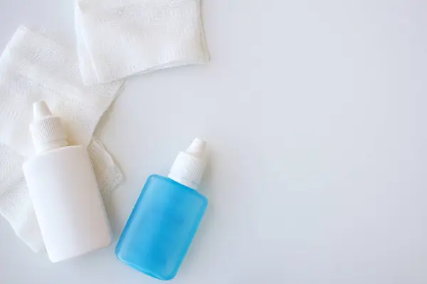 İki tıbbi sıkılabilir plastik şişe ve beyaz arka planda bandaj gazlı bez kopyası için yer var. Beyaz ve mavi göz damlaları.