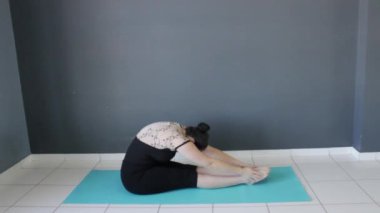 Bayan fitness eğitmeni bacak esnetme için öne eğiliyor. Paschimottanasana yoga pozu veriyor. Mat, stüdyoda pilates yapıyor..