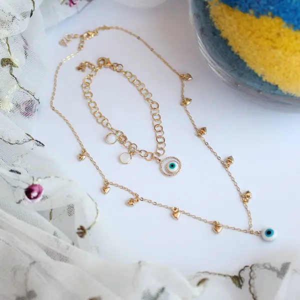 Beyaz arka planda Yunan gözü olan altın kolye ve bilezik. Korunma ve şans tılsımı görevi gören kadın mücevherleri..