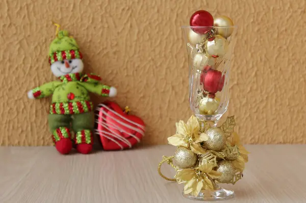 Zarif bir Noel dekoru, içinde kırmızı ve altın xmas toplarıyla dolu bir kristal bardak ve arkada yeşil yün kıyafetli doldurulmuş bir kardan adam oyuncağı, kalp şeklinde bir mücevher..