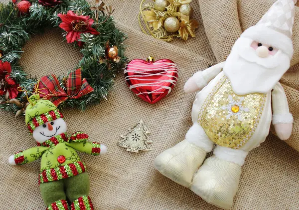 Noel Baba, Noel bayramı kutlamaları için aralık ayında beyaz ve altın rengi kıyafetler giyiyor. Doldurulmuş kardan adam, çelenk ve takı süslemesi. Arka planda Jute kumaşı.