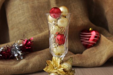 Kristal bardak, kırmızı ve altın Noel toplarıyla dolu şampanya kadehi. Kış mevsimi aralık bayramı kutlaması için sofistike Xmas dekorasyonu. Noel mücevherleri.