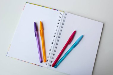 Beyaz arka planda dört renkli kalemli boş sayfa defteri. Yaratıcı kırtasiye malzemeleri, ofis malzemeleri, sanat dersi, okula dönüş konsepti..