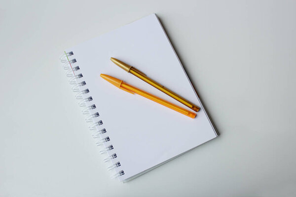 Two golden ballpens on top of a blank page paper spiral notebook. Color stationery, creative writing, authorship, drawing lesson, back to school concept.