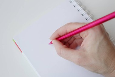 Boş sayfa defterine pembe tükenmez kalemle beyaz insan eli yazısı. Ofis malzemeleri, el yazısı etkinliği, hatırlatma notları, içerik oluşturma kavramı.