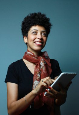 Kahverengi tenli neşeli kadın elinde tabletle yukarı bakıyor. Üniversite dersi, üniversite öğrencisi, şirket hostesi. Stüdyo çekiminde kadın modelin dikey portresi.