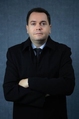 Çapraz kollu, siyah paltolu, kendinden emin bir iş adamı. Şirket işleri, kış mevsimi, ofis işleri ve istihdam için ideal kopya alanı olan dikey stüdyo portresi.