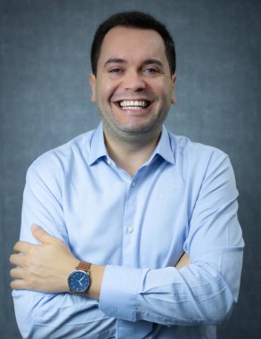 Çapraz kollu, mavi gömlekli, gülen ve kameraya bakan mutlu bir iş adamı. Şirket işleri için mükemmel, kariyer terfisi, ofis işi, yönetici ya da CEO. Mavi arkaplanda kopya alanı olan stüdyo portresi.