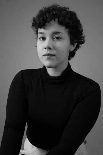 Kısa kıvırcık saçlı ve boş suratlı genç bir kadının siyah beyaz portresi. Gen Z kimliği, kadınlık ve bireysellik kavramları için ideal.