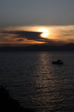 Günbatımı İspanya 'nın Akdeniz' inde yansıyor. Küçük bir tekne ve güzel bir ağaç var. Arka planda ise güzel bir günbatımı var.