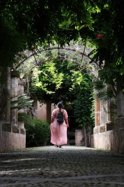 Kadın bahçelerde yürüyor, çeşmeler ve Gotik tarzdaki eski yapılarla.