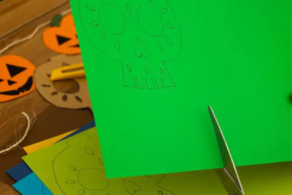 Makas, yeşil bir kağıdı kesiyor. Ölüler gününden kalma bir kafatası var. Evde zanaat var.