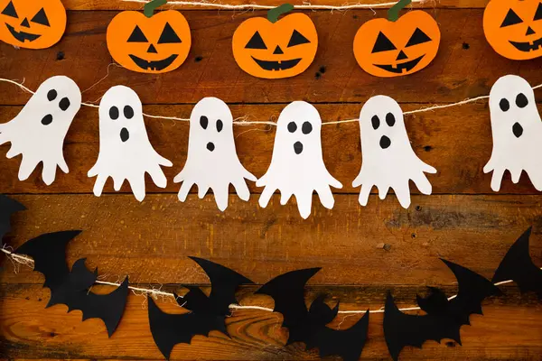 Paper strings with figures of ghosts, pumpkins and bats on a wooden background
