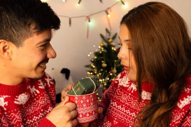 Genç mutlu çift, Noel arifesinde bir Noel bardağının içindeki güzel hediyeyi paylaşıyor.