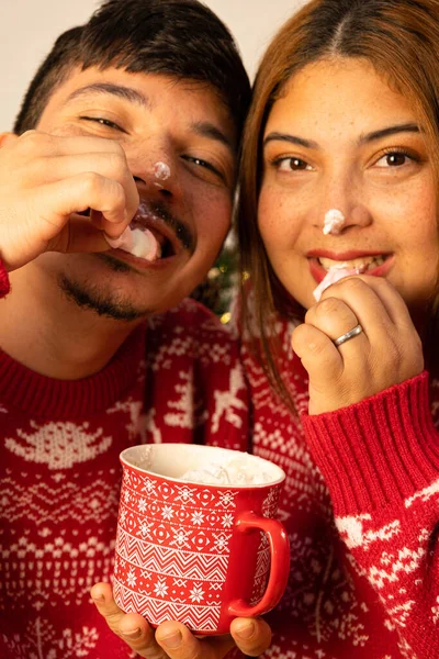Genç ve neşeli bir çift noel arifesinde sıcak çikolatayla marshmallow yiyor.