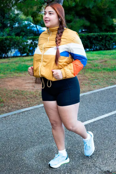 stock image young woman jogging on a rainy day in the morning, she is wearing a yellow waterproof jacket