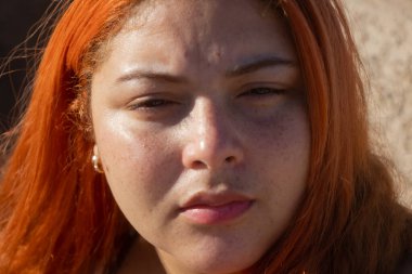 Sabit, endişeli ve düşünceli bir yüzü olan, yüzünde parlak renkleri olan kızıl saçlı bir kız.