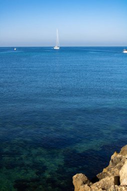 İç kısımlarını görebileceğimiz deniz manzarası. Kayalar ve deniz bitkileri. Uzakta birkaç kıyı botu.