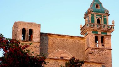 Valldemossa Belediye Müzesi günbatımında doğanın çevresindeki hareketliliğe odaklanmış durumda. Arka planda mavi bir gökyüzü var.