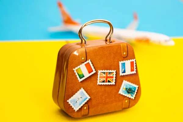 Sarı ve mavi arkaplanlı kahverengi bavul. Arka planda uçak, seyahat ve turizm kavramı var.