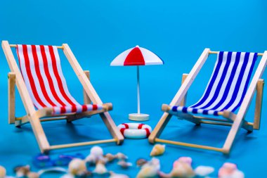 Ortasında kırmızı şemsiye olan iki kırmızı ve mavi hamağı kapatın. Mavi arka plan, plaj tatili konsepti.