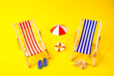 Minyatür parmak arası terlikleri olan iki mavi ve kırmızı hamağın odak noktası sarı arka planda üstten görünüyor.