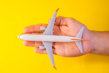 Sarı arka planda üst görüşe sahip bir uçağı tutan erkek el, uçuş ve seyahat kavramı