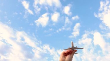 El, arka planda bulutlar, seyahat ve uçuş konsepti olan mavi gökyüzünde dikey olarak minyatür beyaz bir uçağı hareket ettiriyor.
