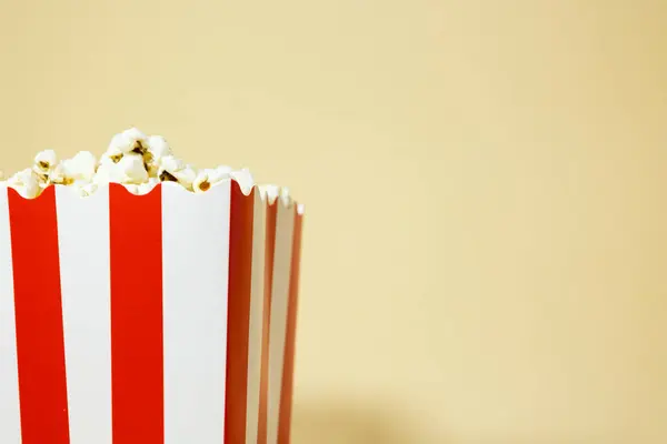 Patlamış mısırı kırmızı karton bir kovayla kapat. Arka planda beyaz çizgiler, sinema yemeği konsepti.