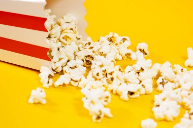 Sarı arka planda dağınık patlamış mısırlı karton kovayı kapat, sinema yemeği konsepti.