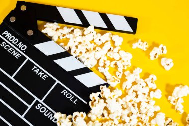 Sarı arka planda patlamış mısırlı siyah beyaz film alkışını kapatın. Sinema eğlence konsepti.