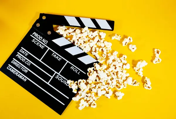 Sarı arka planda patlamış mısır, film yapım ve eğlence konsepti olan siyah beyaz tahta film alkışlarının üst görüntüsü