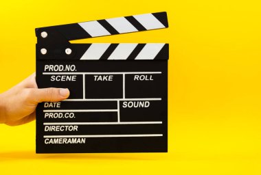 Erkek el, sarı arka plan, yapım ve sinema kavramında siyah ahşap bir film alkışını tutuyor.