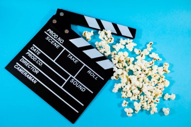 Mavi arka planda patlamış mısır, film yapımı ve eğlence kavramı olan siyah-beyaz tahta film alkışları.