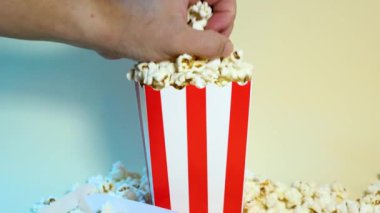 Erkek el, beyaz ve kırmızı karton kovadan bir avuç patlamış mısır alıyor. Yanında 3D gözlükler, sinema ve eğlence konsepti.