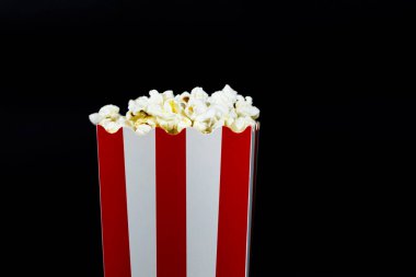 Kırmızı ve beyaz karton kovada patlamış mısır siyah arka planda yakın plan görüntü, sinema yemeği ve eğlence konsepti