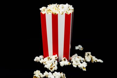 Siyah zemin üzerinde kırmızı ve beyaz bir karton kovada patlamış mısır, yatay görüntü, patlamış mısır ve sinema konsepti