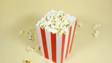 Erkek el, beyaz ve kırmızı bir karton kovayı tutuyor. Krem rengi izole bir arka planda patlamış mısır var.