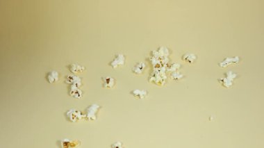 Erkek el, beyaz ve kırmızı bir karton kovayı izole edilmiş krem rengi arka plana patlamış mısırla yerleştiriyor.