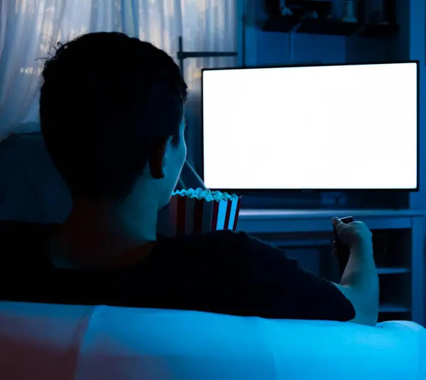 Adam gece televizyon izlerken oturma odasında patlamış mısır yiyor. Televizyon izleyen adam kavramı.