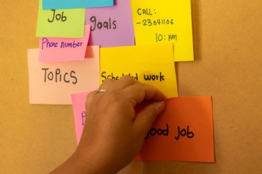 Bir tahtaya çok renkli kağıtlara notlar yapıştıran kadın el yazısı, not kavramı ve çalışma örgütü