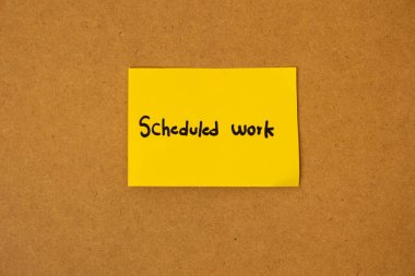 Üzerinde planlanmış çalışmaların yazılı olduğu sarı yapışkan not kağıdı, kahverengi bir tahtaya yapışıp kalmış, iş organizasyonu kavramı.