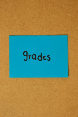 Üzerinde notların yazılı olduğu mavi yapışkan not kağıdının dikey görüntüsü, kahverengi tahtaya yapışmış, notlar konsepti