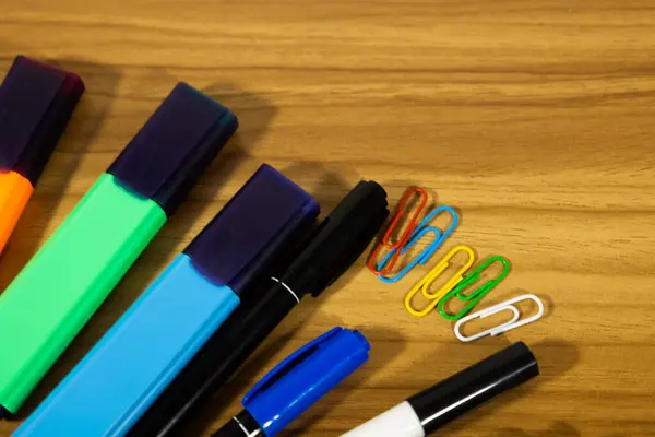 Kalemler, fosforlu kalemler ve tahta arka plana dağılmış çeşitli renklerde klipler. çalışma materyalleri