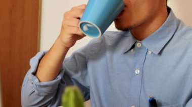 İşadamı, sabahları ofiste laptopuyla çalışırken mavi bardaktan kahve içiyor.