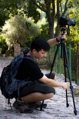 Etrafı doğa ile çevrili kayalık bir yolda fotoğrafçı tripodu fotoğraf çekmeye ayarlıyor.