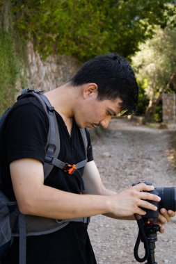 Genç maceracı, köyün ortasında kayalık bir yolun ortasında kamerayla fotoğraf çekiyor.