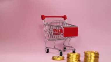 Erkek, altın sikkeleri pembe izole bir zemin üzerinde bir alışveriş arabasına koyuyor. Tasarruf konsepti ve evde ekonomi.