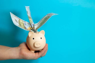 Mavi izole bir zemin, ekonomi ve finans kavramına dayanan banknotlarla dolu bir kumbarayı elinde tutan bir erkek.