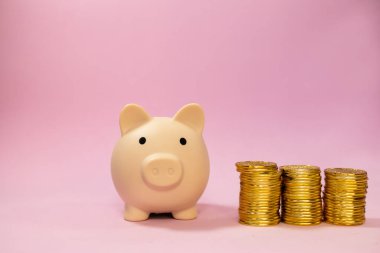 Pembe izole edilmiş arka planda birikmiş altın paralarla dolu bir kumbara. Fotokopi alanı, tasarruf kavramı.